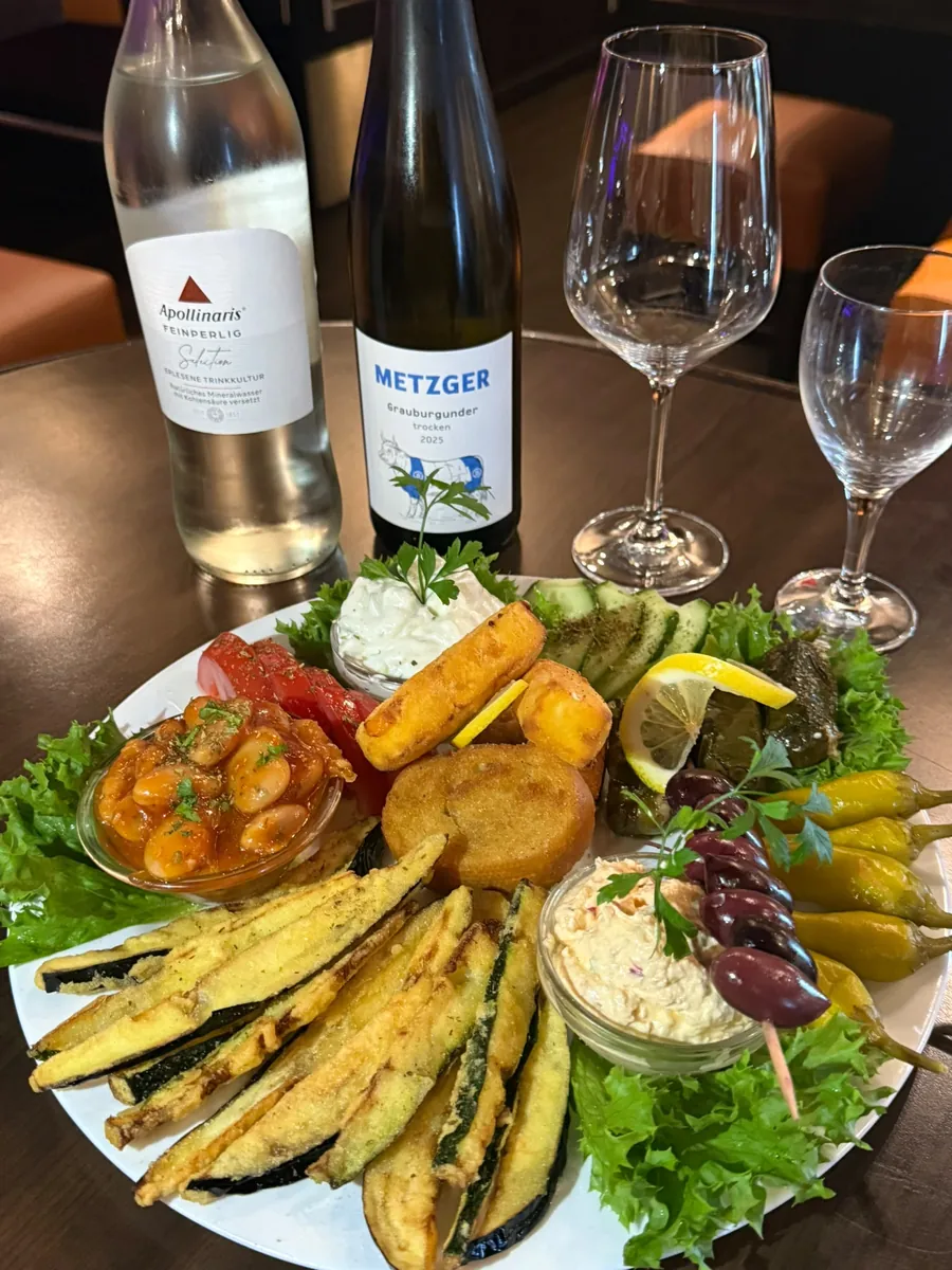 Tapas-Teller für zwei im Gleis Drei mit gebackenem Gemüse, Bohnen in Tomatensoße, Tzatziki, Dolmades und Oliven, dazu eine Flasche Wein und eine Flasche Wasser